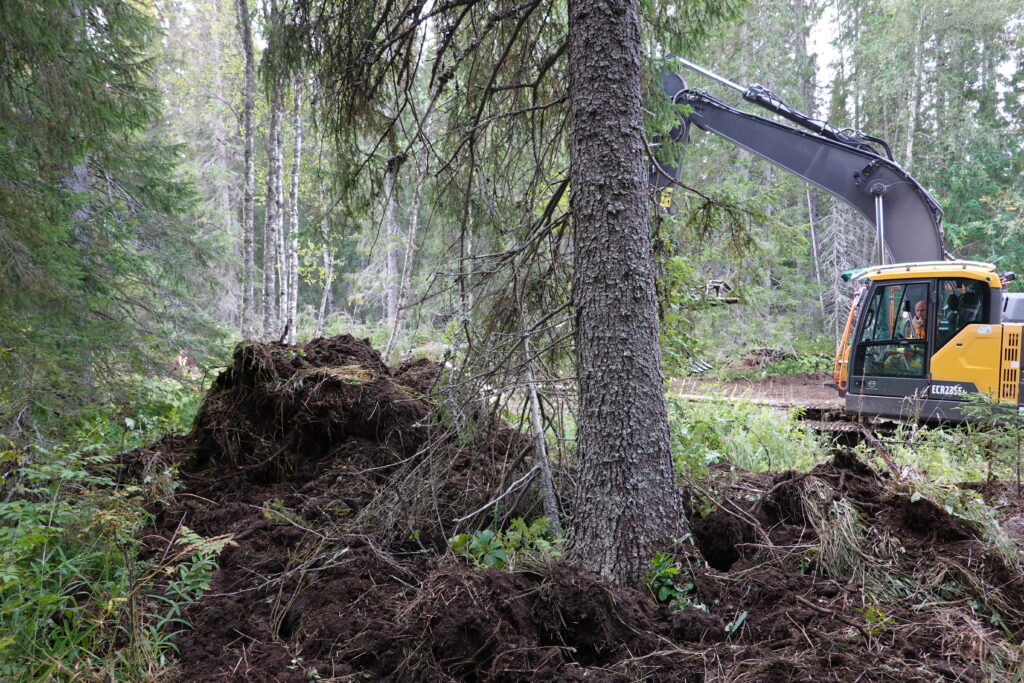 Soil cover in a large pile by the stream. With an excavator in the background. 