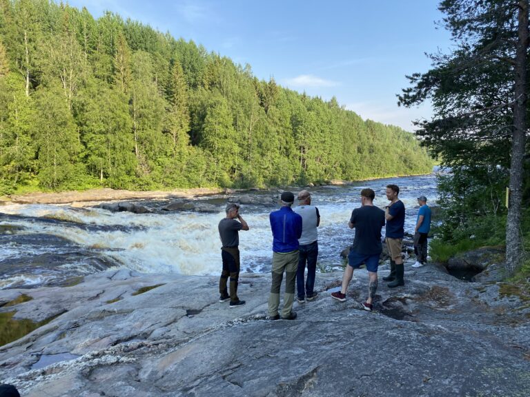 Sex män står i grupp och studerar en fors.